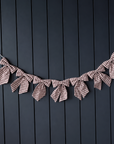 Seven muted cranberry and cream striped cotton bows draped as a garland against a dark panelled wall
