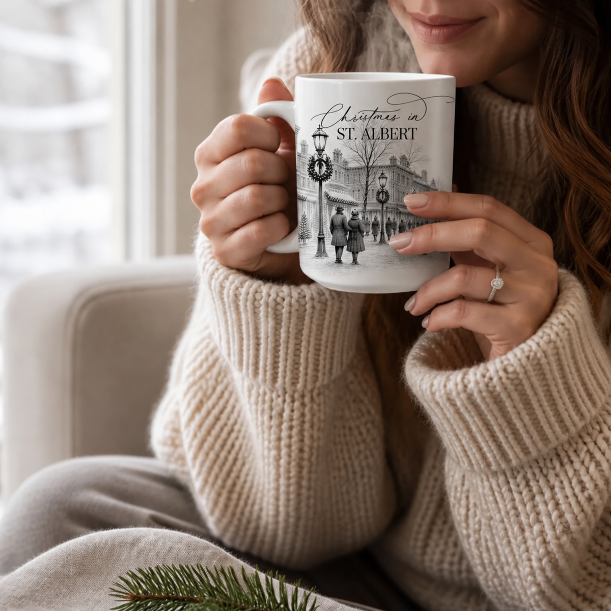 Woman in a cream knit sweater holding a Christmas in St. Albert mug with a festive town illustration beside a window.