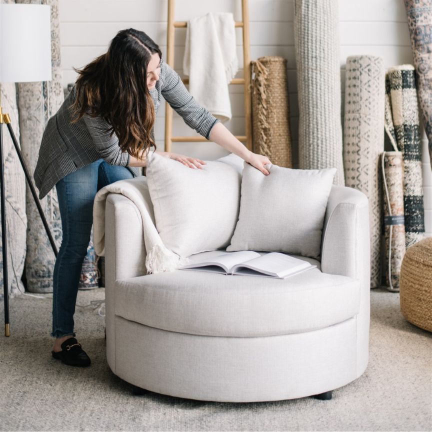 interior designer arranging pillows on a gray cuddle chair in a room with decorative rugs in St. Albert